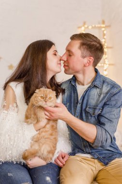 Genç güzel çift ile kedi parlak odasında yatağın üstüne oturuyor