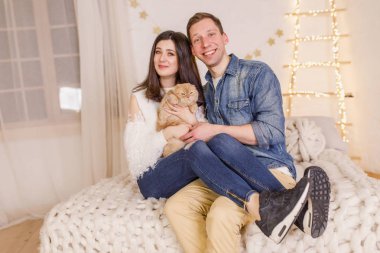 Genç güzel çift ile kedi parlak odasında yatağın üstüne oturuyor