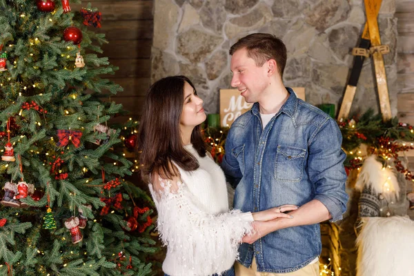 Young beautiful couple is standing near the fireplace on the background of the Christmas tree and smiling