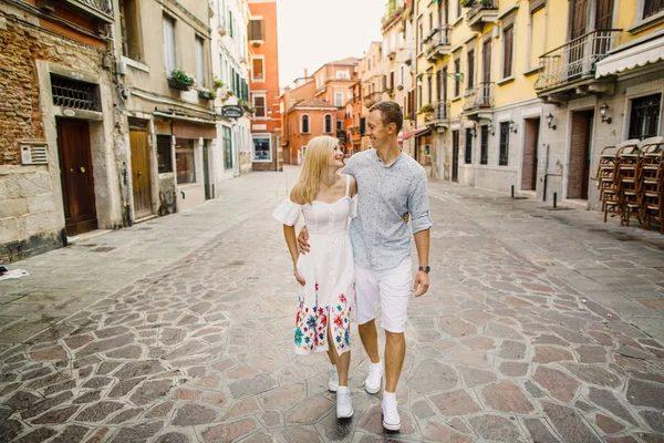 Young beautiful couple girl in dress man in white shirt walk through the streets of Venice Italy