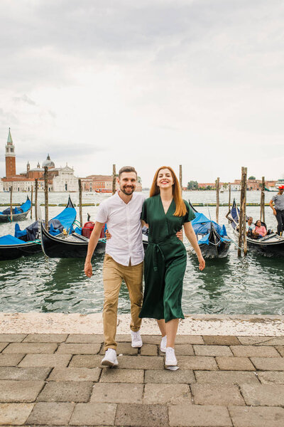 Young beautiful couple girl in a green dress a man in a white shirt walk near the water overlooking the Grand Canal in Venice Italy