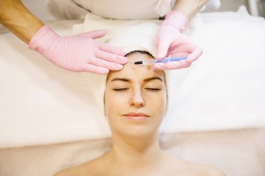 Güzellik salonunda genç bir kıza yüz maskesi takan bir kadın..