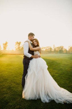 Mutlu evlilik çifti çimlerin üzerinde sarılıp öpüşüyor.