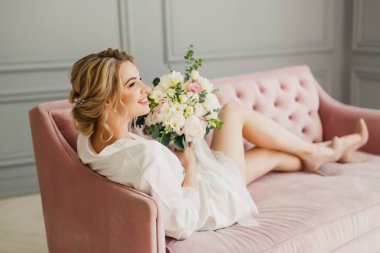 genç güzel düğün gelin pembe bir yatakta parlak bir odada oturuyor ve gülümseyen