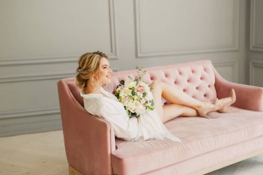 genç güzel düğün gelin pembe bir yatakta parlak bir odada oturuyor ve gülümseyen