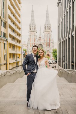 genç güzel çift gelin ve damat şehirde kilisenin arka plan üzerinde yürümek ve gelin damat şık giyinmiş güzel bir elbise içinde gülümse