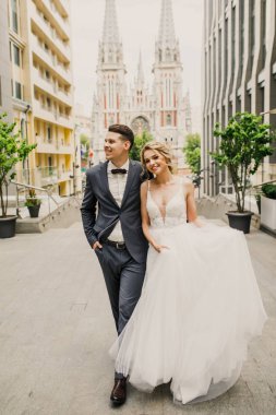 genç güzel çift gelin ve damat şehirde kilisenin arka plan üzerinde yürümek ve gelin damat şık giyinmiş güzel bir elbise içinde gülümse
