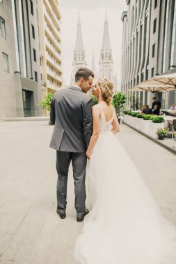 genç güzel çift gelin ve damat şehirde kilisenin arka plan üzerinde yürümek ve gelin damat şık giyinmiş güzel bir elbise içinde gülümse