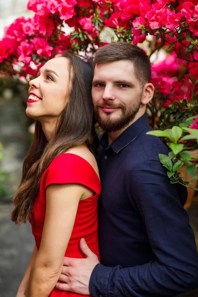 若いです美しいですカップルの女の子で赤いドレス男で青いシャツは花と庭に立つ — ストック写真