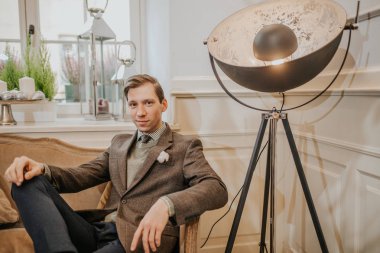 Genç adam gündelik giysiler içinde yerde oturuyor ve kameraya bakıyor.