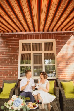 Çekici genç gelin ve damat kahve içip arka planda kafede oturuyorlar.