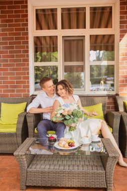 Çekici genç gelin ve damat kahve içip arka planda kafede oturuyorlar.