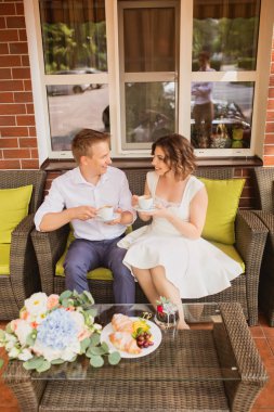 Çekici genç gelin ve damat kahve içip arka planda kafede oturuyorlar.