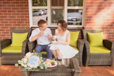 Çekici genç gelin ve damat kahve içip arka planda kafede oturuyorlar.