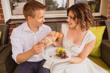 çekici genç gelin ve damat kafenin arka planında lezzetli kruvasanlar yiyorlar.