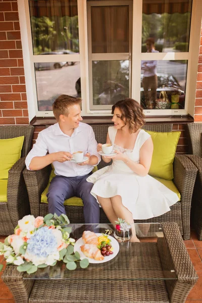 Çekici genç gelin ve damat kahve içip arka planda kafede oturuyorlar.