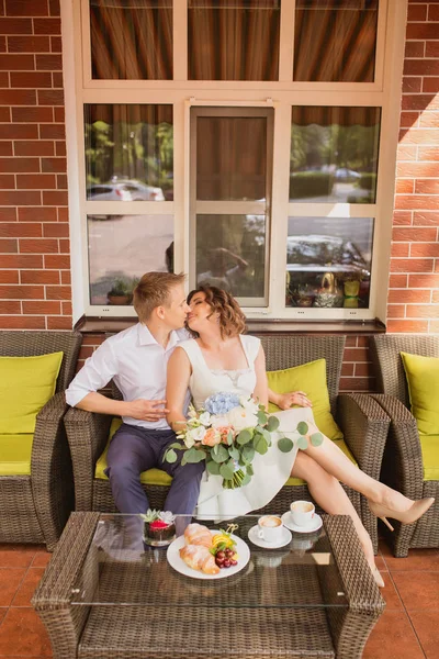 Çekici genç gelin ve damat kahve içip arka planda kafede oturuyorlar.