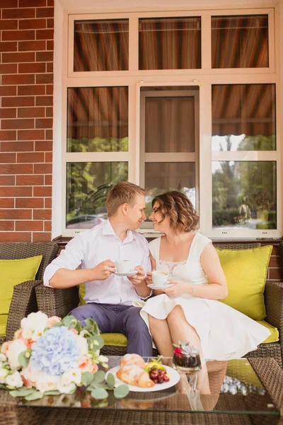 Çekici genç gelin ve damat kahve içip arka planda kafede oturuyorlar.