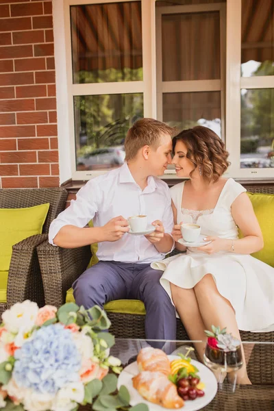 Çekici genç gelin ve damat kahve içip arka planda kafede oturuyorlar.