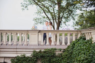 Güzel genç gelin ve damat bahçe manzaralı mermer merdivenlerde yürüyor ve poz veriyorlar.