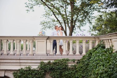 Güzel genç gelin ve damat bahçe manzaralı mermer merdivenlerde yürüyor ve poz veriyorlar.