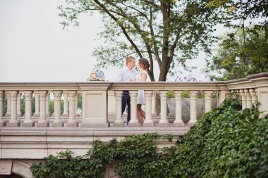 Güzel genç gelin ve damat bahçe manzaralı mermer merdivenlerde yürüyor ve poz veriyorlar.