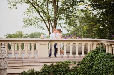 Güzel genç gelin ve damat bahçe manzaralı mermer merdivenlerde yürüyor ve poz veriyorlar.