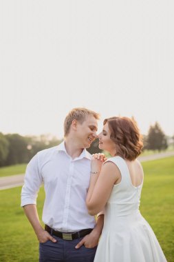 Güzel genç damat ve gelin yemyeşil çimen manzaralı yeşil parkta yürüyor.