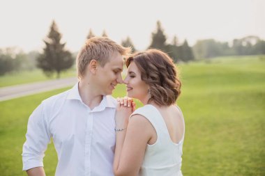 Güzel genç damat ve gelin yemyeşil çimen manzaralı yeşil parkta yürüyor.