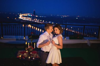 Genç aşıklar aşk buluşmasını kutluyor ve köprü üzerinde şarap kadehleriyle dikiliyorlar.