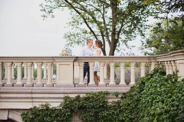 Güzel genç gelin ve damat bahçe manzaralı mermer merdivenlerde yürüyor ve poz veriyorlar.
