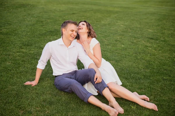 若い花嫁と新郎が緑豊かな緑の芝生の上に座って庭の景色を背景に — ストック写真