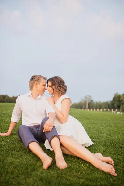 若い花嫁と新郎が緑豊かな緑の芝生の上に座って庭の景色を背景に — ストック写真