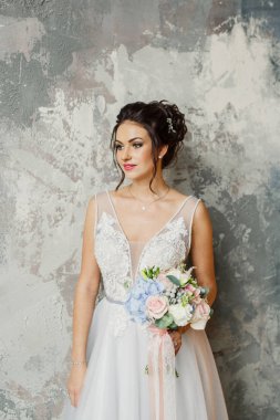 Gri bir arka planda güzel bir elbiseyle genç ve güzel bir gelinin portresi.