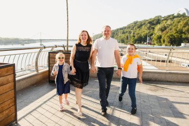 Genç aile babası anne ve kız gün batımında parkta yürüyorlar ve eğleniyorlar.