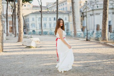 beyaz giysiler içinde genç güzel kız gün batımında İtalya'da Roma'da yürüyor