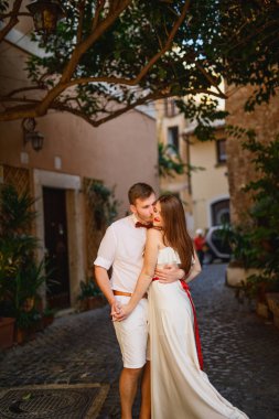 beyaz giysiler içinde genç güzel çift gün batımında İtalya'da Roma'da yürüyor