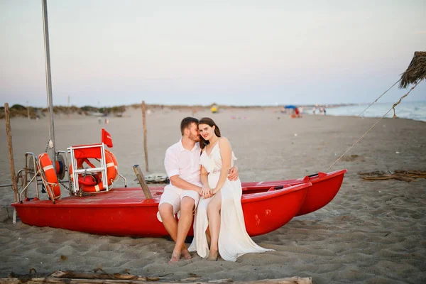 Fiatal Szép Pár Fehér Ruhában Áll Egy Piros Hajó Strandon — Stock Fotó