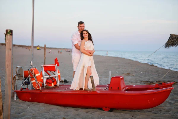 Fiatal Szép Pár Fehér Ruhában Áll Egy Piros Hajó Strandon — Stock Fotó