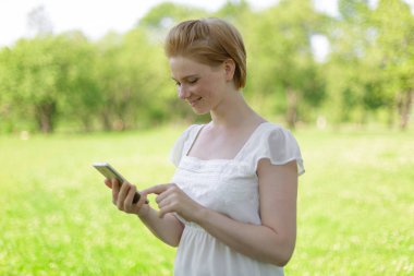 Sevimli kadın sıcak bahar gününde parkta otururken cep telefonu hoş metin mesajı okuyor,muhteşem kadın müzik dinliyor ve cep telefonu bilgi arıyor