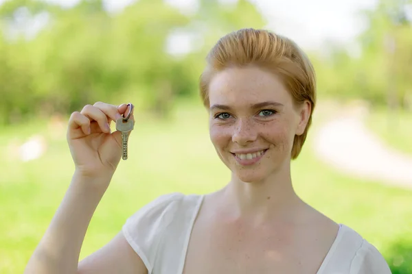 Real estate. Happy broker. Attractive young woman holding keys while standing outdoor against park