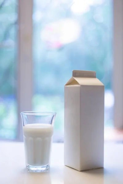 Boîte en carton et verre de lait sur la table dans la cuisine — Photo