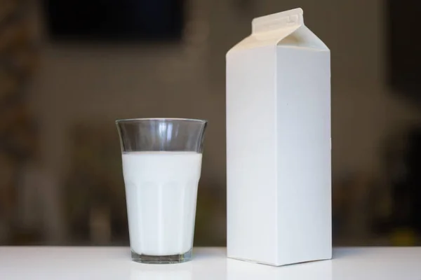 Caja de cartón y vaso de leche en la mesa en la cocina —  Fotos de Stock