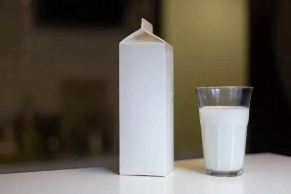 Caja de cartón y vaso de leche en la mesa en la cocina — Foto de Stock