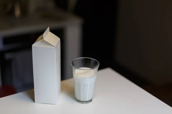 Kartonnen doos en glas melk op tafel in de keuken — Stockfoto