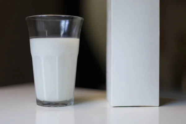 Pudełko kartonowe i szklanka mleka na stole w kuchni — Zdjęcie stockowe