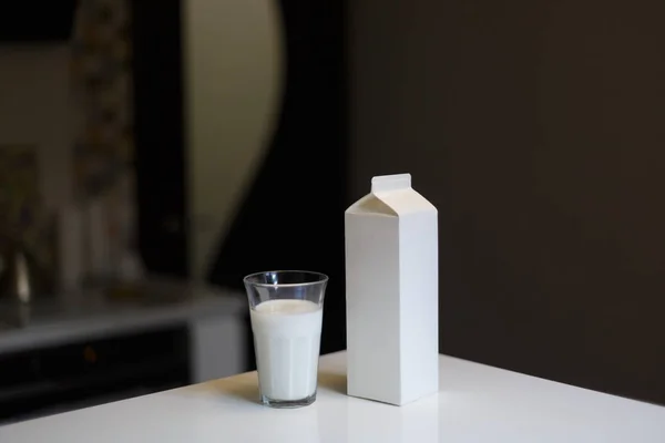 Caja de cartón y vaso de leche en la mesa en la cocina —  Fotos de Stock