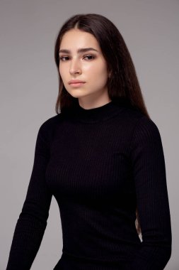 Gri arka planda siyah elbiseli güzel bir kadın.