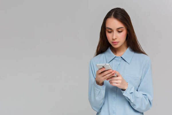 Содержит подростка с длинными волосами, держит современный мобильный телефон, перемещается по социальным сетям, имеет жизнерадостное выражение, изолирован на сером фоне, получает сообщение