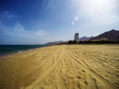 Çölde okyanus kıyısında kumlu bir sahil ve uzakta bir bina.